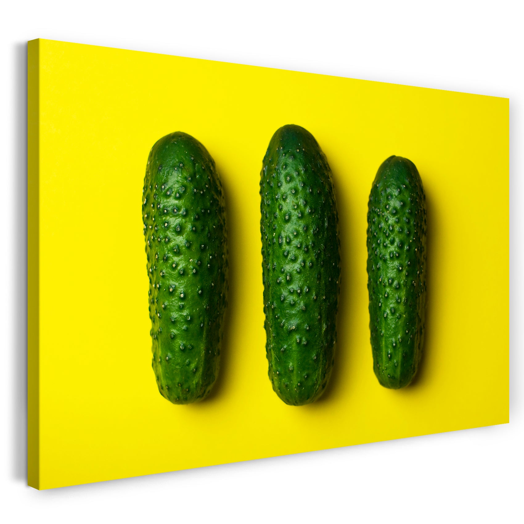 Leinwandbild Essensbilder Gemüse drei Gurken vor gelbem Hintergrund