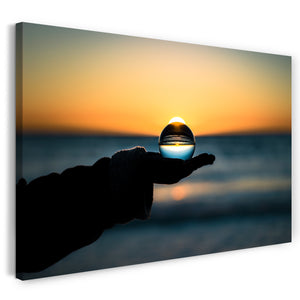 Leinwandbild Landschaftsbilder Glaskugel in Hand vor Meer und Sonnenuntergang