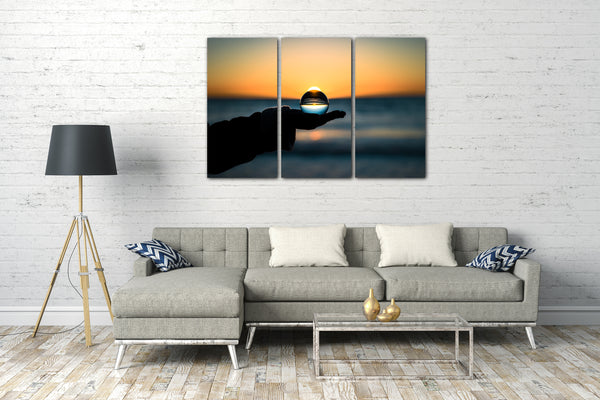 Leinwandbild Landschaftsbilder Glaskugel in Hand vor Meer und Sonnenuntergang