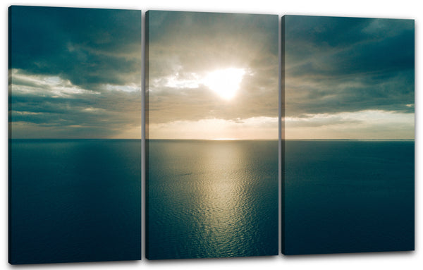 Leinwandbild Sonnenuntergang zwischen Wolkendecke über dunkel-blaues Meer