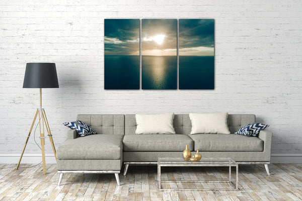 Leinwandbild Sonnenuntergang zwischen Wolkendecke über dunkel-blaues Meer