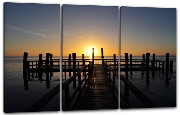 Leinwandbild Holzsteg im Meer unter aufgehender Sonne