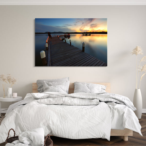 Leinwandbild Holz-Steg mit weißen Pfahl-Spitzen, Boot und Sonnenuntergang im Hintergrund