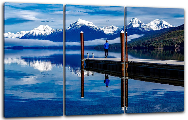Leinwandbild Mann auf Steg am See, schneebedeckte Berge und spiegelnder See